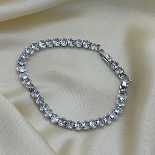 A silver-tone tennis bracelet adorned with clear round-cut crystals, displayed on a draped cream satin fabric background.