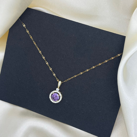 A round purple crystal pendant with a clear stone halo on a fine gold chain, styled on a dark grey card.
