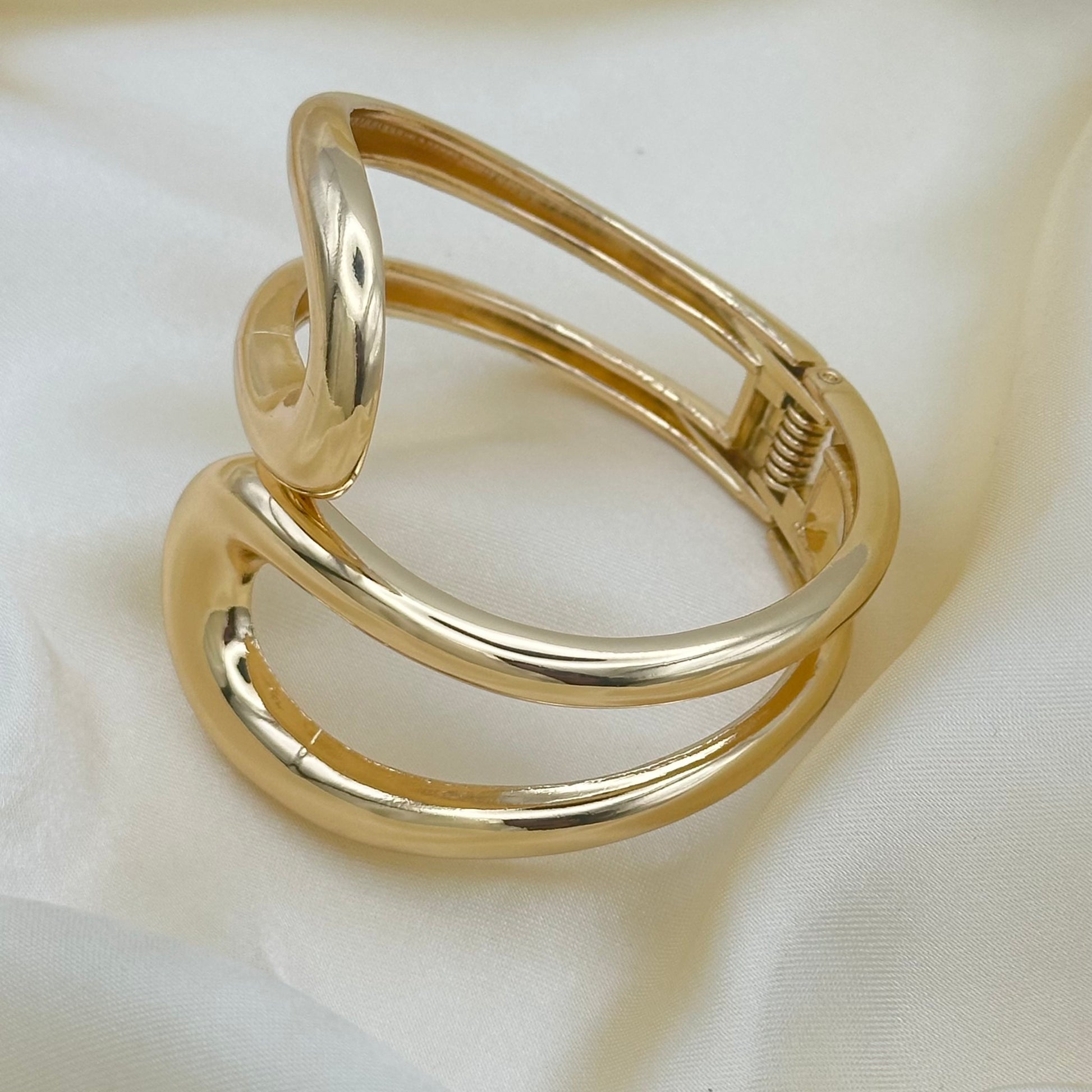 A polished gold-toned metal wrap ring with a spring-loaded clasp, displayed on a draped white fabric background.