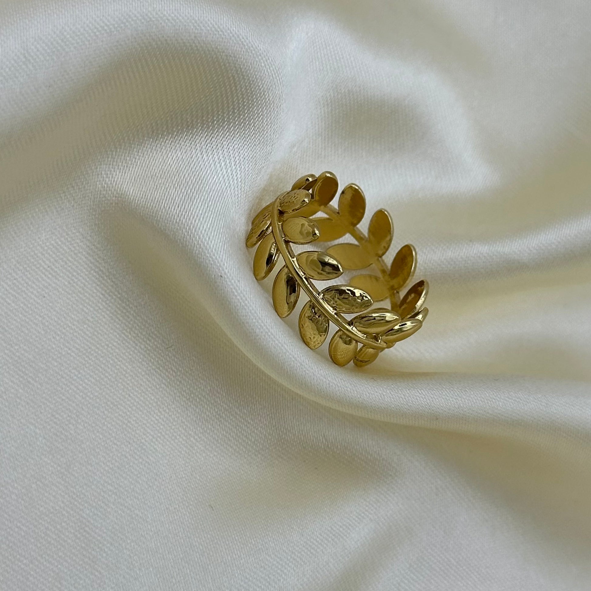 Close-up of a gold laurel leaf band ring on draped cream satin fabric.