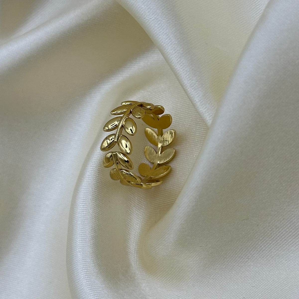 An adjustable open gold laurel leaf ring standing upright on cream satin, showing the wraparound branch design.