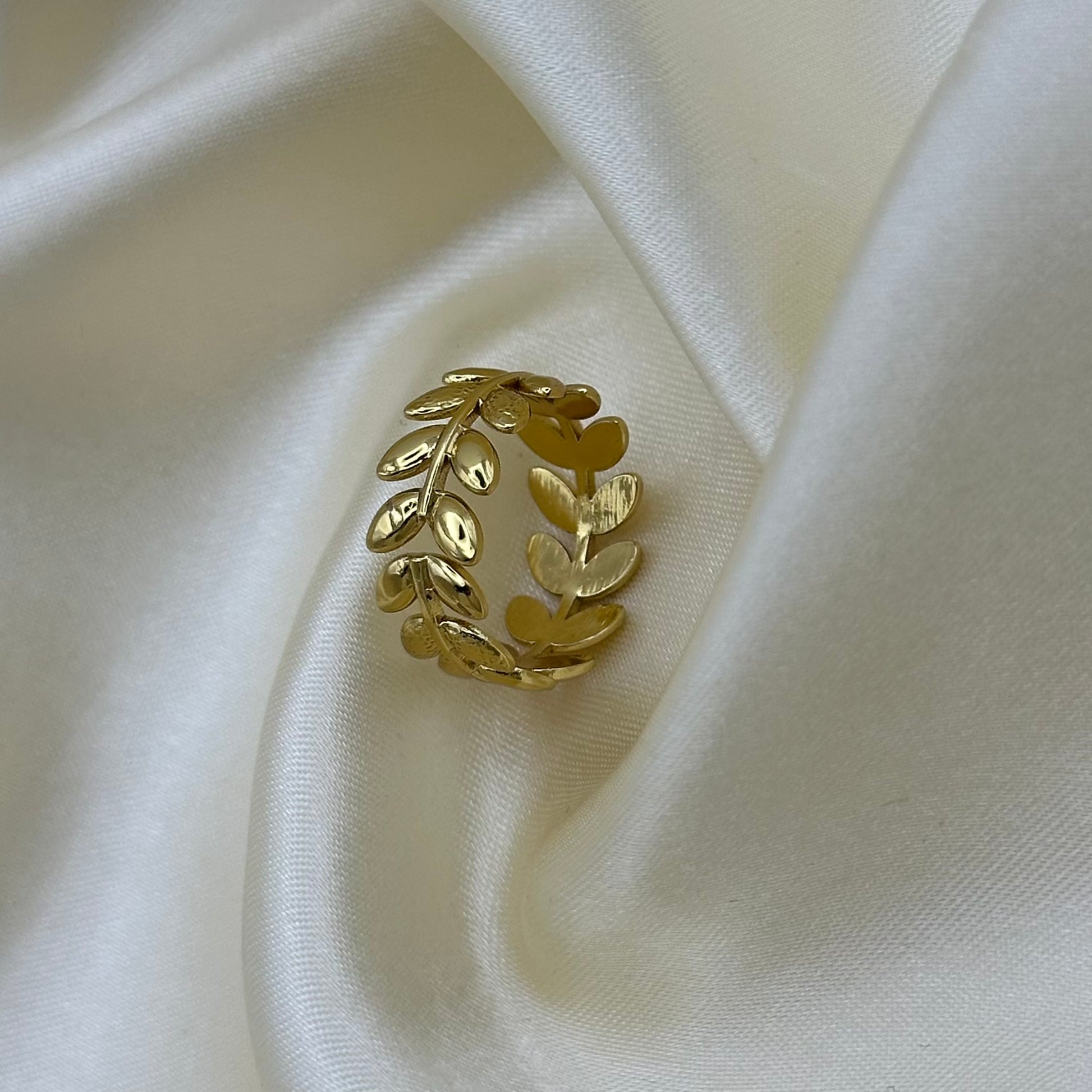 An adjustable open gold laurel leaf ring standing upright on cream satin, showing the wraparound branch design.