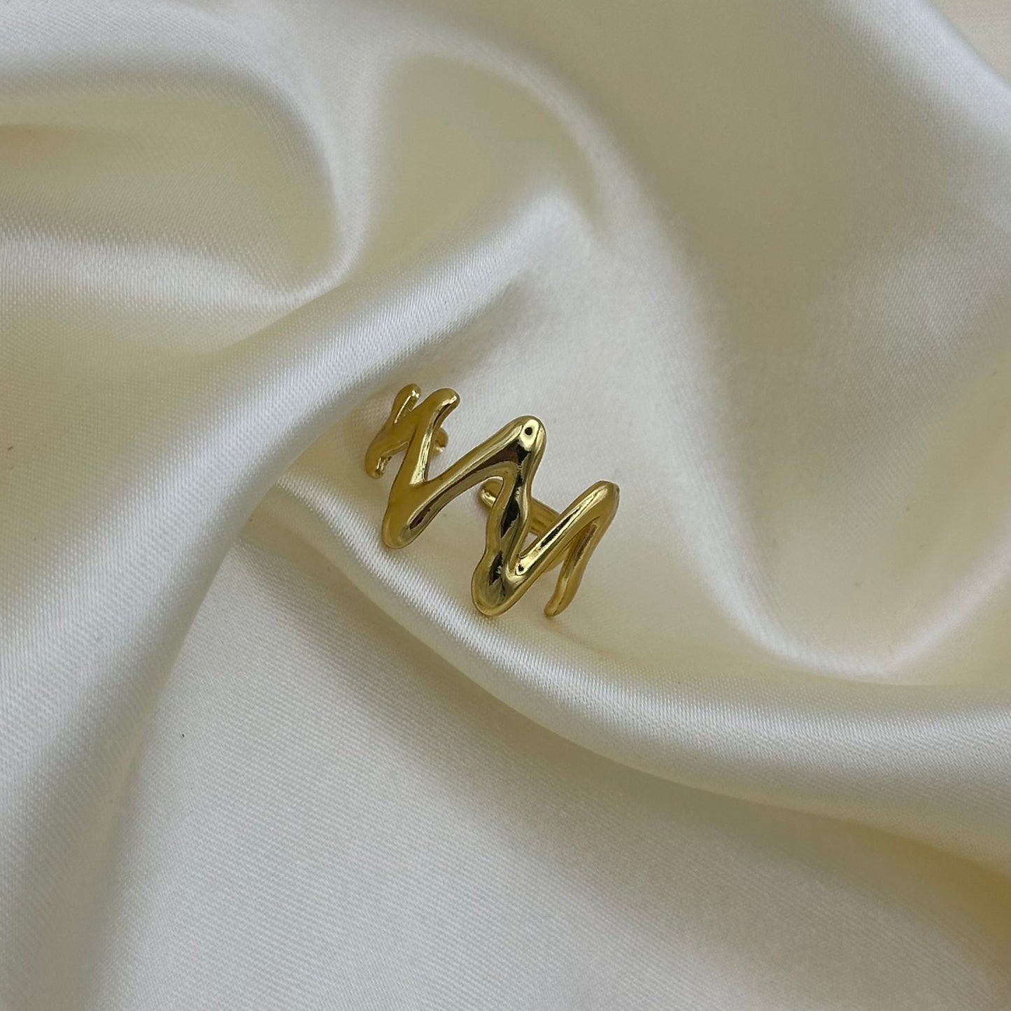 A polished gold wavy ring set against a draped cream satin fabric background.