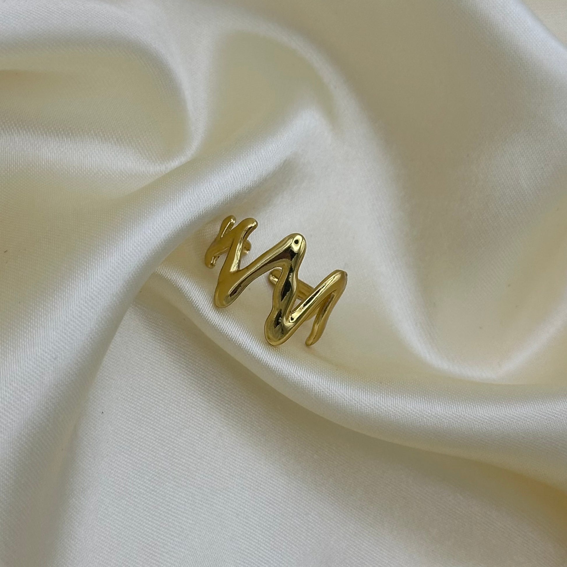 A polished gold wavy ring set against a draped cream satin fabric background.