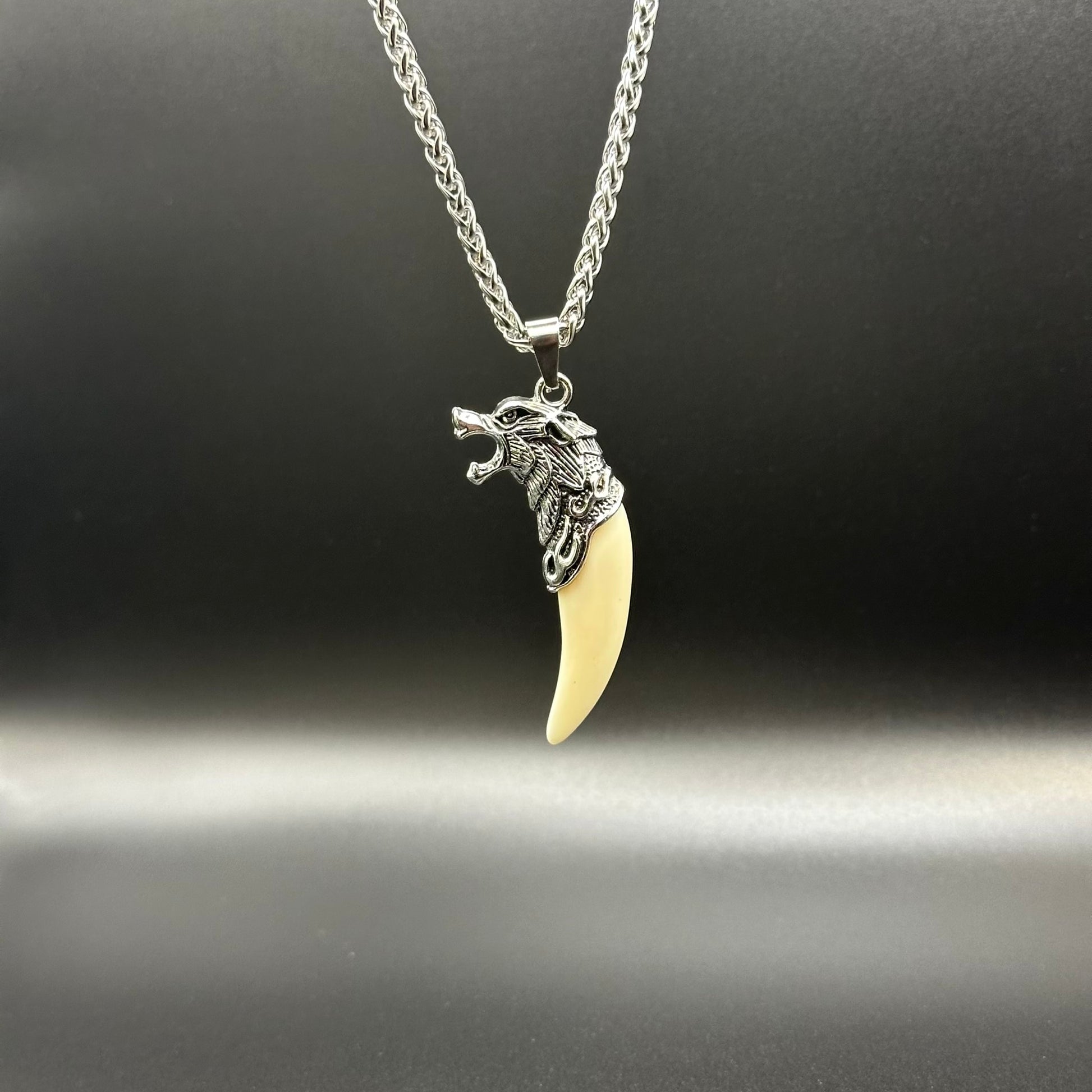 A silver wolf head pendant necklace with a curved ivory-colored tooth charm, displayed on a dark gray background.