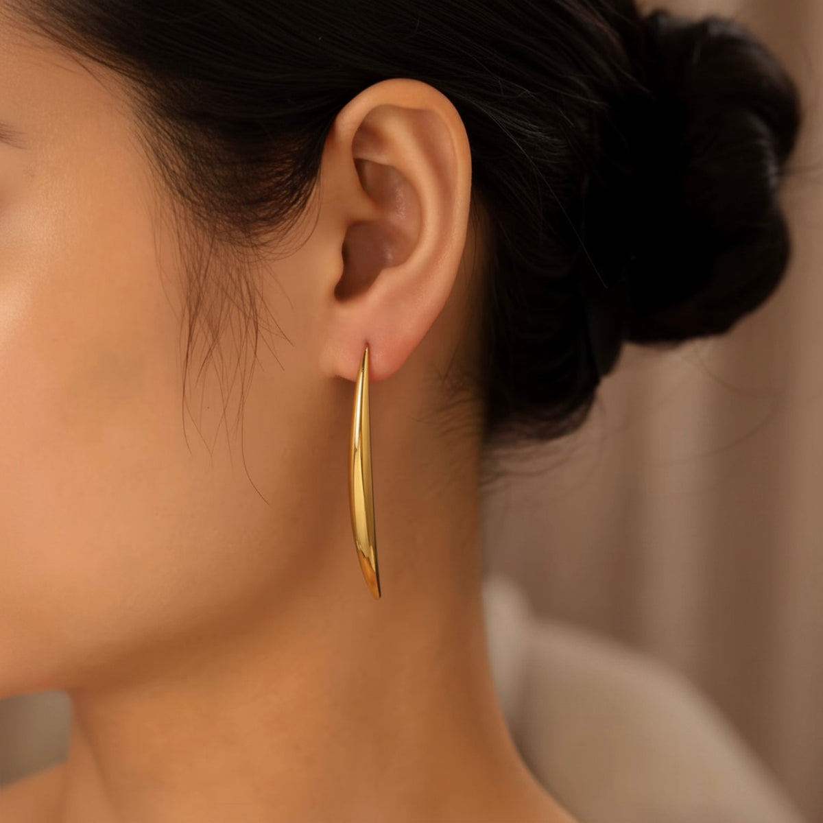 A close-up side profile of a woman wearing a single thin, polished gold hoop earring.
