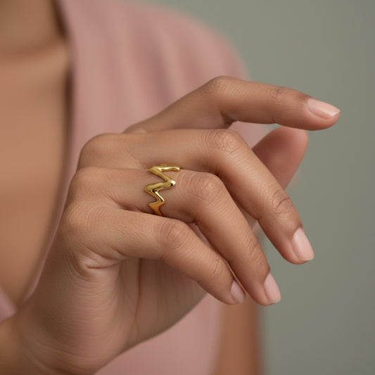 A gold-colored, abstract zigzag open ring displayed on a cream-colored satin fabric.